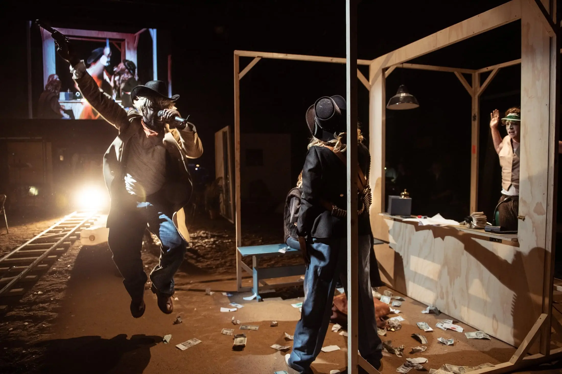 A cowboy leaps through the frontier town set, backlit, papers scattered on the floor