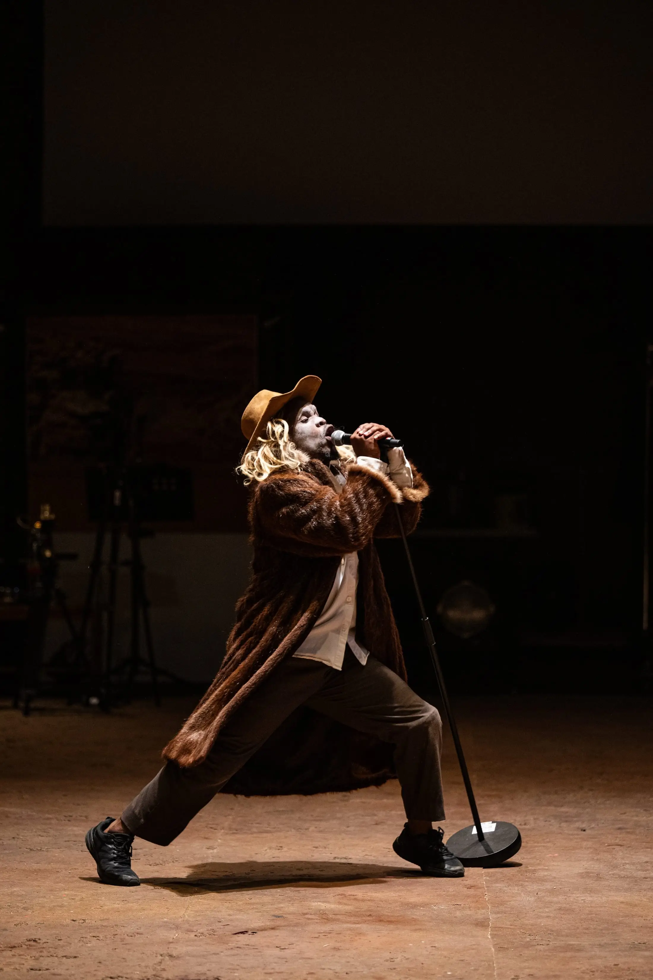 A Dark Noon performer in whiteface and a frontier hat, mid-stride on a dusty stage