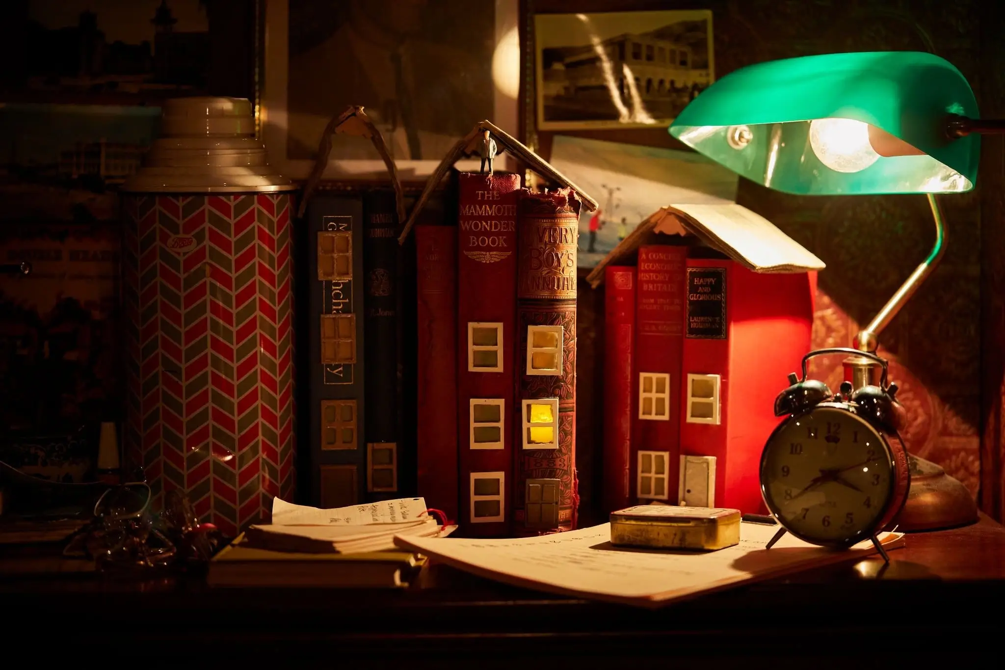 Books, a green lamp and an alarm clock on the library desk