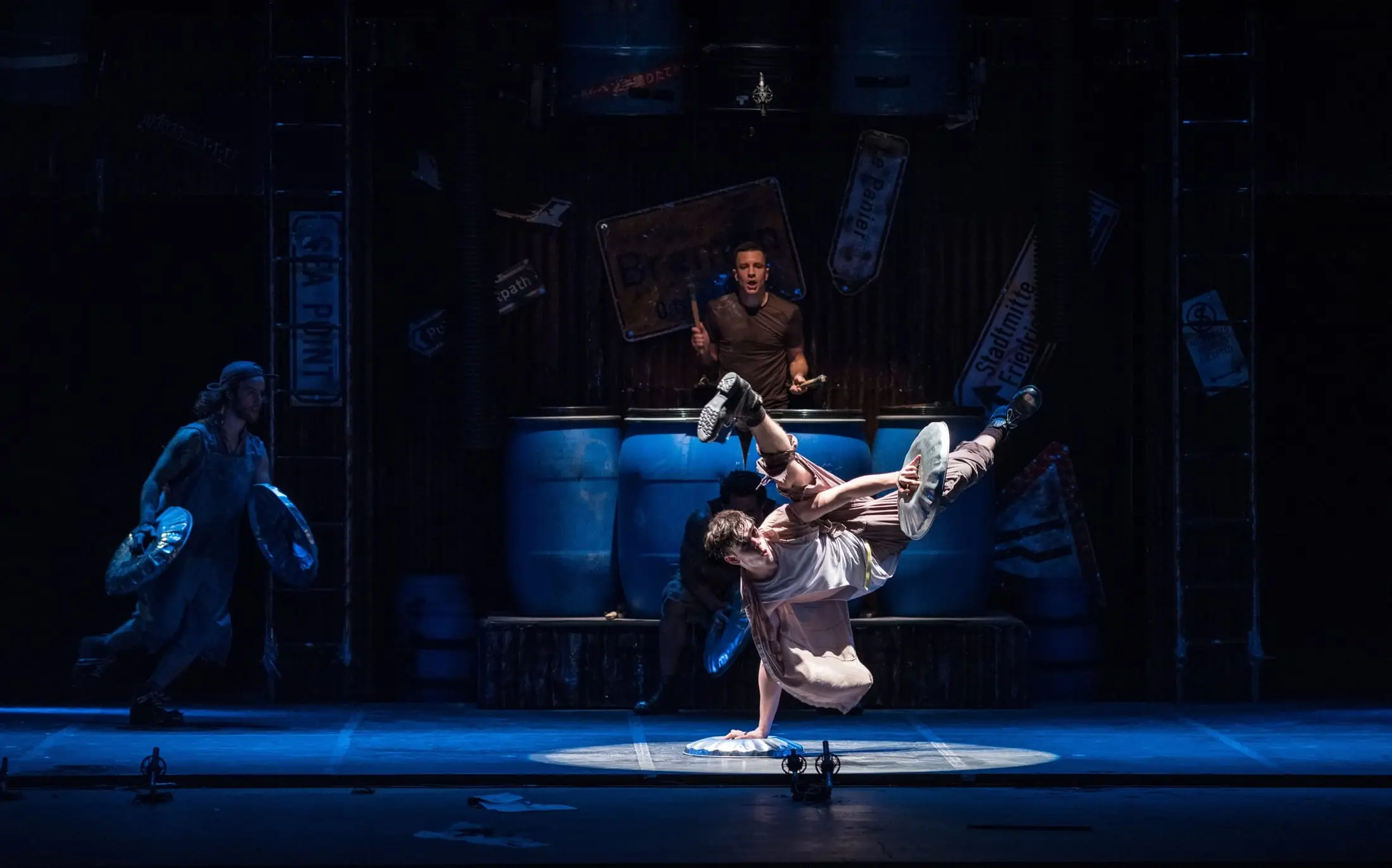 A performer balanced on one hand on a dustbin lid