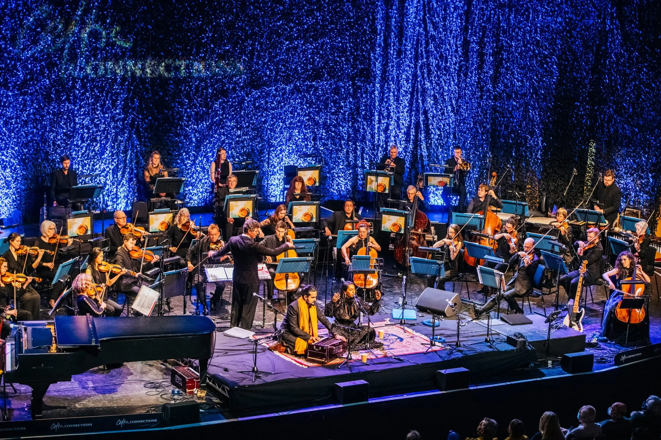 The orchestra and choir on stage at Celtic Connections under blue light