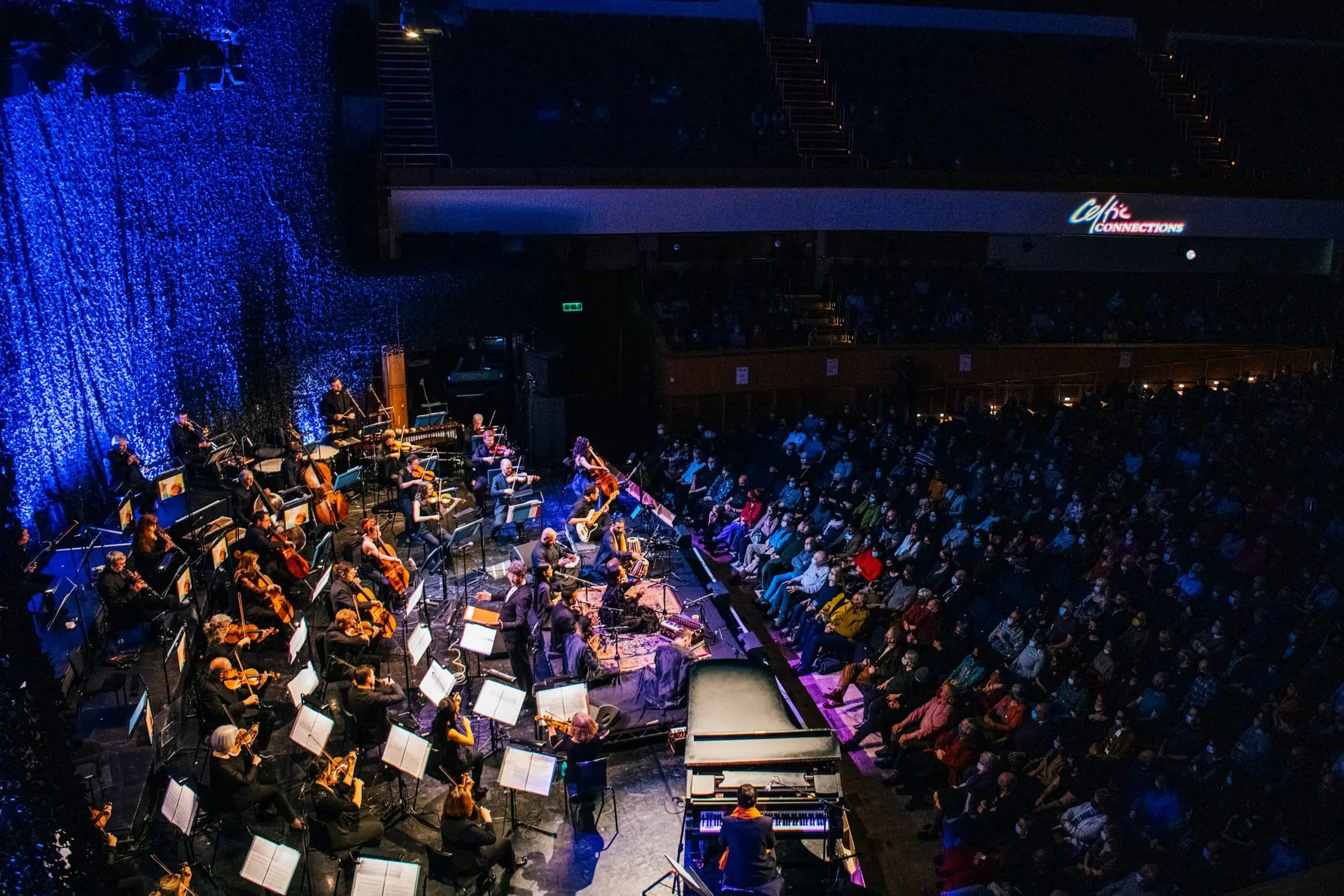 The orchestra seen from above, the hall lit blue