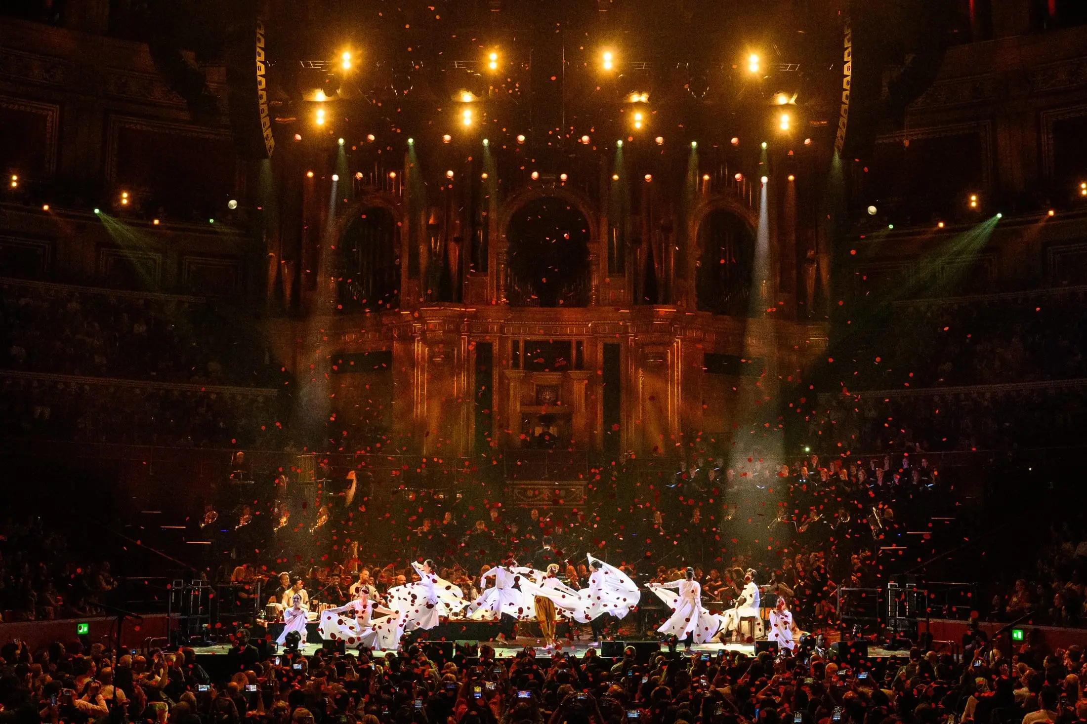 The full ensemble on stage at the Royal Albert Hall in golden light